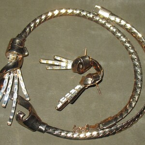 May include: A gold-tone necklace with a twisted design and clear crystal accents. The necklace is paired with matching earrings.