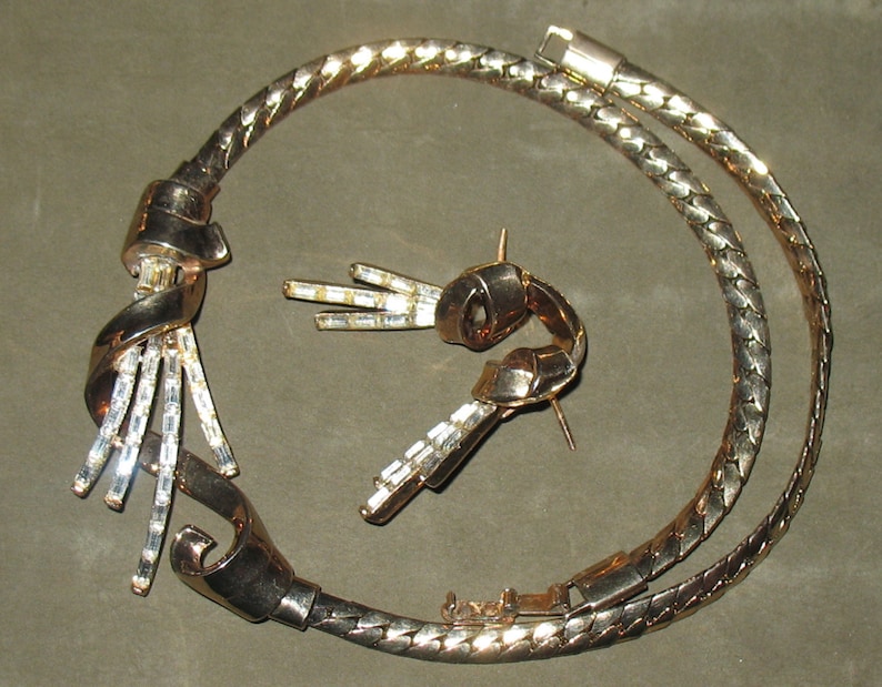 May include: A gold-tone necklace with a twisted design and clear crystal accents. The necklace is paired with matching earrings.
