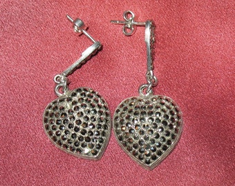 May include: A pair of silver heart-shaped earrings with black crystal accents. The earrings have a dangling design and are perfect for adding a touch of sparkle to any outfit.