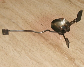 May include: A metal camping stove with a round, bowl-shaped base and three legs. The stove is made of silver metal and has a simple design.