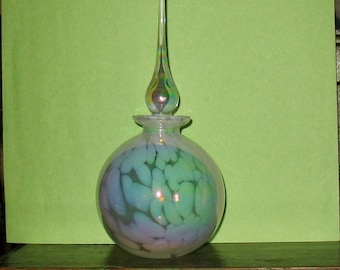 May include: A clear glass bottle with an iridescent stopper and a swirling pattern of white and green.