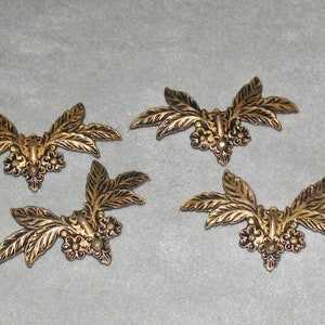 May include: Four gold-colored metal leaf and flower embellishments. Each embellishment features a central cluster of three small flowers with a raised center, surrounded by two sets of three leaves.