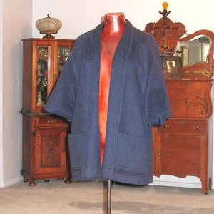 May include: A navy blue, open-front jacket with wide sleeves and two front pockets. The jacket is displayed on a red mannequin, showcasing its tailored design and relaxed fit. The jacket's fabric appears to be a medium-weight wool or wool blend.