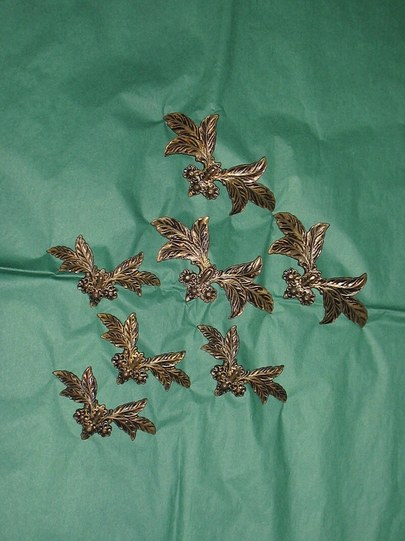 May include: Eight gold-colored metal leaf-shaped embellishments with small flower details. The embellishments are arranged in a triangular pattern on a green background.