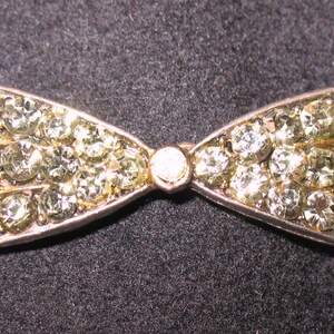May include: A silver bow brooch with clear rhinestones.