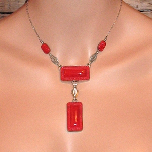 May include: A silver chain necklace with red glass rectangular pendant drops. The necklace has two smaller red glass beads on each side of the pendant.