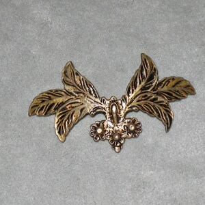 May include: Gold-toned metal leaf design with a cluster of small, round, raised details in the center.