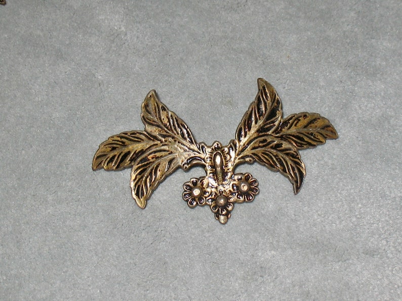 May include: Gold-toned metal leaf design with a cluster of small, round, raised details in the center.