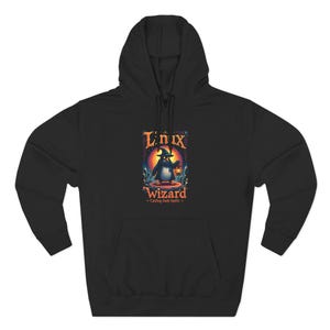 May include: Black hoodie with a front pocket. The front graphic shows a penguin wizard holding a lantern, with the text "Linux Wizard - Casting Soda Spells". The design uses blue, orange, and yellow colours.