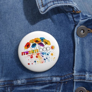 May include: A white button with a colorful design featuring a rainbow of paint splatters and flowers with the text "mmm bop" in the center.