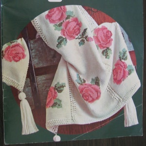 May include: A book titled "Afghans" with a cover featuring a white crocheted blanket with pink roses and green leaves. The blanket has tassels on the edges. The book is from Columbia-Minerva and is book number 742.