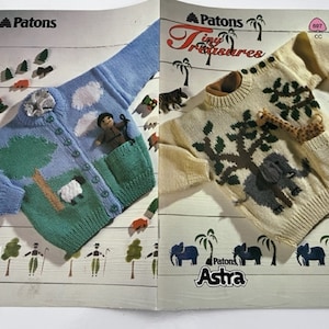 May include: A knitting pattern booklet featuring two children's sweaters. The first sweater is blue with a green tree, a white sheep, and white clouds. The second sweater is cream with a brown tree, a grey elephant, and a giraffe. The booklet is titled "Patons Tiny Treasures" and "Patons Astra".