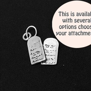 May include: Silver charm featuring two tablets with Hebrew text, a traditional symbol of the Ten Commandments. The charm is attached to a silver loop.