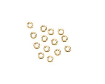 May include: A collection of small, gold-colored jump rings scattered against a white background. These circular rings are designed for jewelry making and crafting. The rings are evenly spaced and appear to be made of metal.