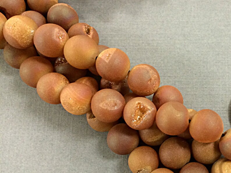 May include: A strand of round, brown agate beads with a slightly rough, textured surface. The beads have a natural, earthy look.