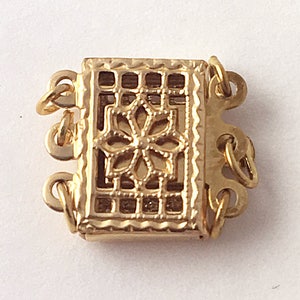 May include: Gold-toned metal clasp with a decorative floral design. The clasp has multiple loops for attaching to a necklace or bracelet.