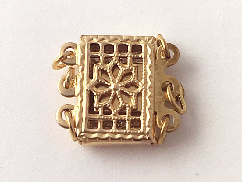 May include: Gold-toned metal clasp with a decorative floral design. The clasp has multiple loops for attaching to a necklace or bracelet.