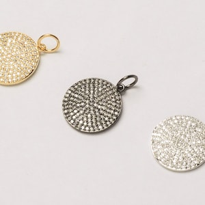May include: Three round pendants with a pave setting of small clear stones. The pendants are in gold, black, and silver.