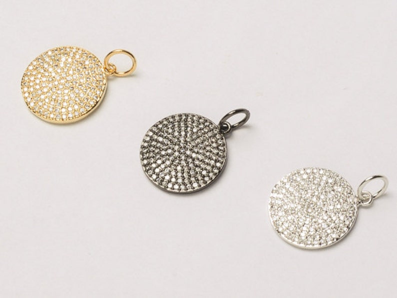 May include: Three round pendants with a pave setting of small clear stones. The pendants are in gold, black, and silver.