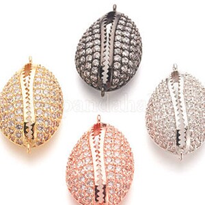 May include: Four oval-shaped bead caps with a decorative design. The caps are made of metal and have a silver, gold, rose gold, and black finish. Each cap is adorned with small, clear rhinestones.