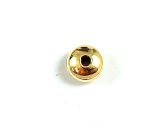 May include: A single, shiny gold-colored bead with a central hole. The bead has a smooth, rounded surface and reflects light, creating highlights. The bead is likely used in jewelry making or crafting.