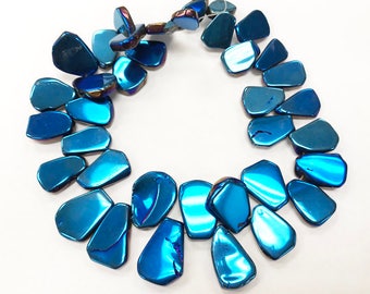 Può includere: Una collana composta da perline blu iridescenti a forma di goccia. Le perline hanno una finitura lucida e riflettono la luce, creando un effetto scintillante. La collana è disposta in un motivo circolare, mettendo in mostra le singole perline.
