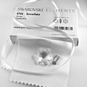 Swarovski Magic Classic Crystal snowflake ornament .A silver snowflake pendant necklace with a clear crystal snowflake charm. The necklace has a white satin ribbon.