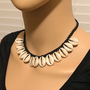 May include: A white shell choker necklace with a black braided cord. The necklace is made of cowrie shells and is approximately 16 inches long.