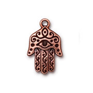 May include: Copper-toned metal charm in the shape of a hamsa hand with an eye in the center. The hamsa is a symbol of protection and good luck.