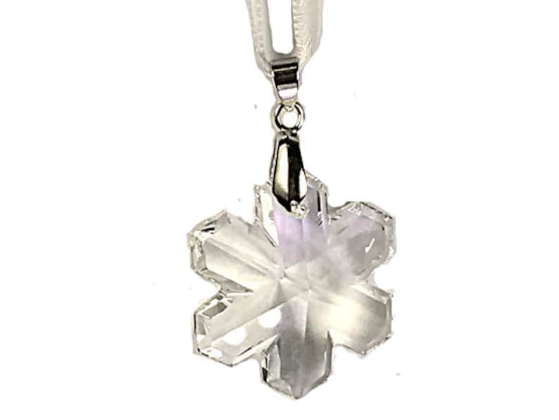 Swarovski Magic Classic Crystal snowflake ornament .A silver snowflake pendant necklace with a clear crystal snowflake charm. The necklace has a white satin ribbon.