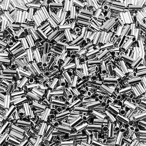 May include: A close-up shot of a pile of shiny, silver-colored metal crimp tubes. The tubes are cylindrical with a hole through the center. The ends are cut at an angle. The tubes are scattered randomly.