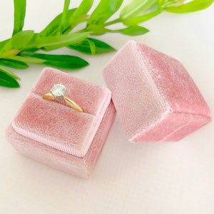 May include: A pink velvet ring box with a gold ring and a clear diamond inside.