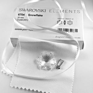 Swarovski Magic Classic Crystal snowflake ornament .A silver snowflake pendant necklace with a clear crystal snowflake charm. The necklace has a white satin ribbon.