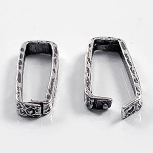 May include: Two silver-toned metal clasps with a textured finish. The clasps are rectangular in shape and have a slightly open design.