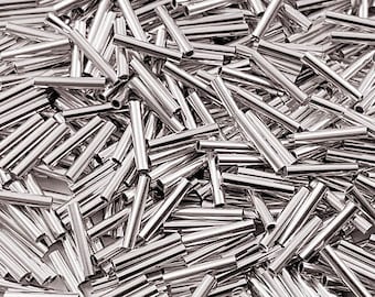 May include: A close-up shot of a pile of shiny, silver-colored metal tubes. The tubes are cylindrical, with a hollow center and open ends. They are scattered randomly, creating a dense, textured pattern. The lighting highlights the metallic sheen.