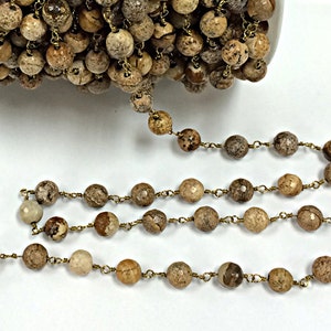 May include: A brown and beige gemstone rosary chain with gold-toned metal accents. The chain is made of round beads and is strung on a wire.