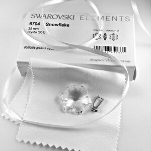 Swarovski Magic Classic Crystal snowflake ornament .A silver snowflake pendant necklace with a clear crystal snowflake charm. The necklace has a white satin ribbon.