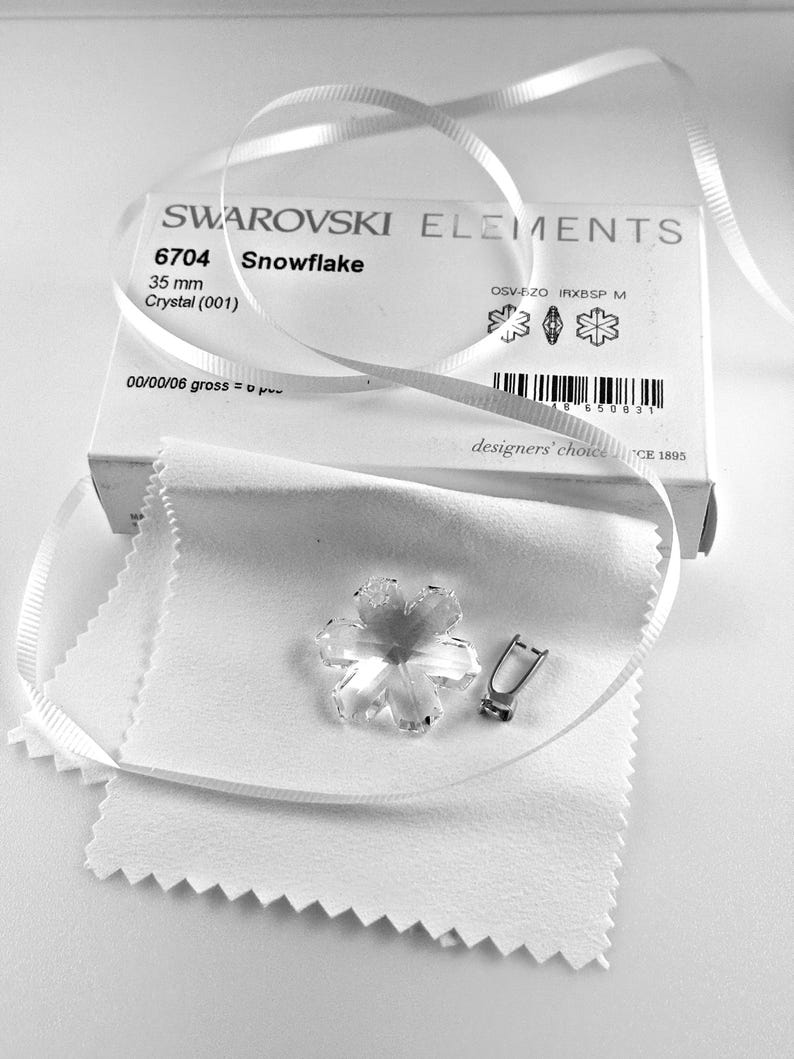 Swarovski Magic Classic Crystal snowflake ornament .A silver snowflake pendant necklace with a clear crystal snowflake charm. The necklace has a white satin ribbon.