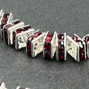 May include: A silver chain with red crystal beads. Each bead is a square with a silver frame and a red crystal center.