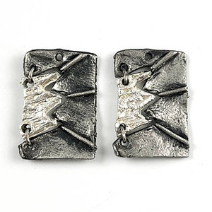 May include: Two silver-toned rectangular earrings with a textured, abstract design. Each earring features a jagged, zigzagging pattern in a lighter silver color, connected by small metal loops.