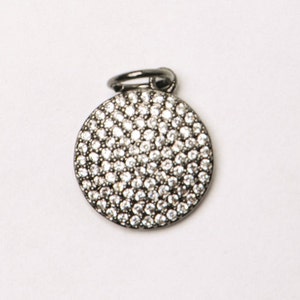 May include: A silver charm with a round, pave-set crystal design.