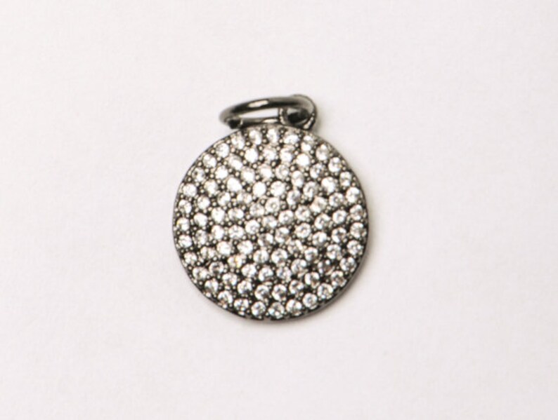 May include: A silver charm with a round, pave-set crystal design.