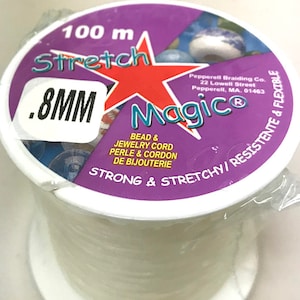 May include: A white spool of 0.8 mm stretch magic bead and jewelry cord. The spool is labeled "100 m Stretch Magic®" and "Strong & Stretchy/Resistente & Flexible".