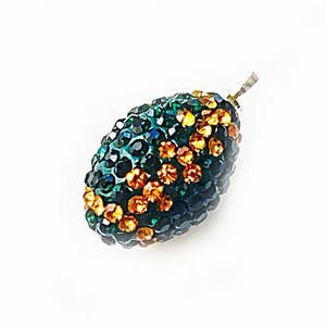May include: A dark green and gold crystal bead with a faceted design. The bead is oval shaped and has a hole for stringing.