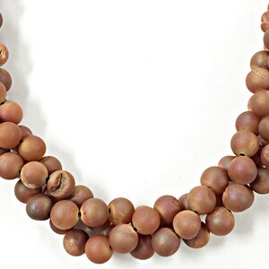 May include: A strand of brown agate beads, each bead is round and smooth. The beads are strung on a clear thread.