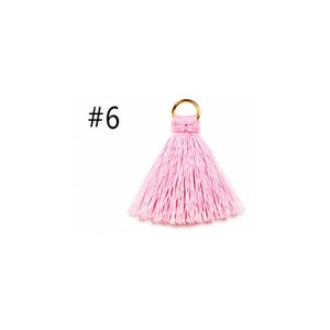 Peut inclure: Un pompon rose clair dot&eacute; d'un anneau m&eacute;tallique dor&eacute; sur le dessus pour la fixation. Le pompon est compos&eacute; de nombreux fils fins verticaux qui s'&eacute;vasent vers le bas. Le chiffre 6 est imprim&eacute; en noir sur la gauche du pompon.