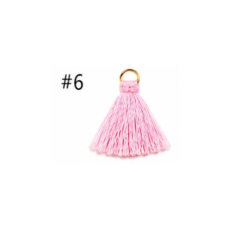 Peut inclure: Un pompon rose clair dot&eacute; d'un anneau m&eacute;tallique dor&eacute; sur le dessus pour la fixation. Le pompon est compos&eacute; de nombreux fils fins verticaux qui s'&eacute;vasent vers le bas. Le chiffre 6 est imprim&eacute; en noir sur la gauche du pompon.