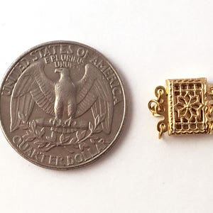 May include: Gold-toned metal clasp with a decorative design. The clasp is about the size of a US quarter.