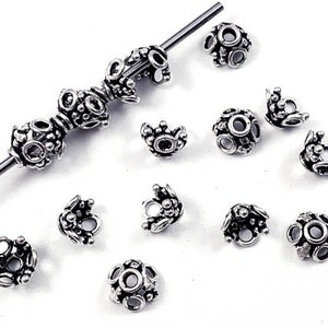 May include: Silver tone metal bead caps with a decorative design. The bead caps are small and have a round shape.