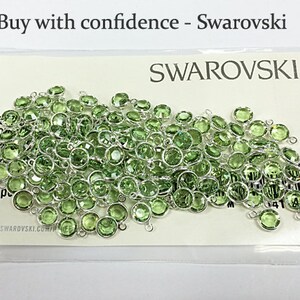 Puede incluir: Primer plano de un paquete de 48 cuentas de cristal verde con lazos plateados. El paquete est&aacute; etiquetado con "SWAROVSKI" y "48 pc".